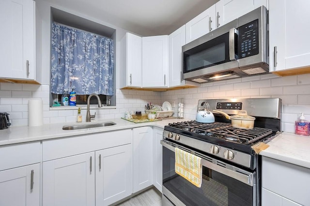 kitchen featuring backsplash, appliances with stainless steel finishes, white cabinets, a sink, and light stone countertops