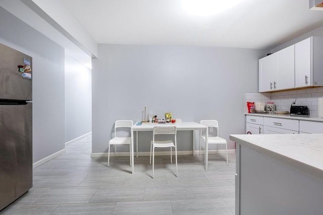 kitchen featuring tasteful backsplash, freestanding refrigerator, light countertops, and white cabinetry