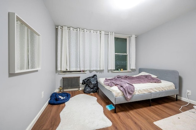 bedroom with radiator, baseboards, and wood finished floors