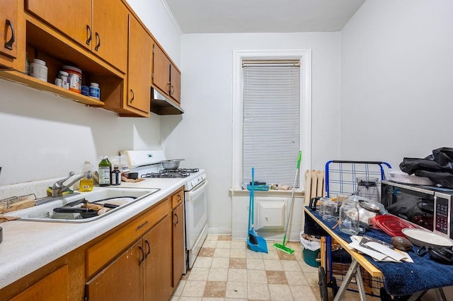 kitchen with a sink, brown cabinetry, light countertops, and gas range gas stove