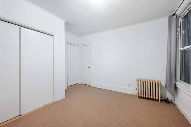 unfurnished bedroom with radiator heating unit, a closet, crown molding, and light colored carpet