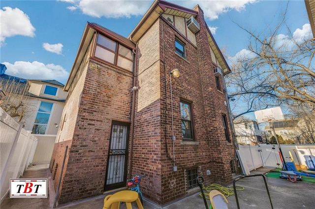 rear view of property featuring a patio, a wall unit AC, a gate, fence, and brick siding