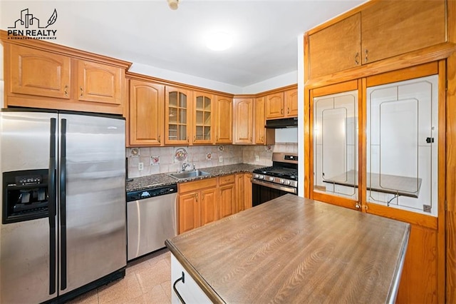 kitchen featuring dark countertops, backsplash, glass insert cabinets, under cabinet range hood, and stainless steel appliances