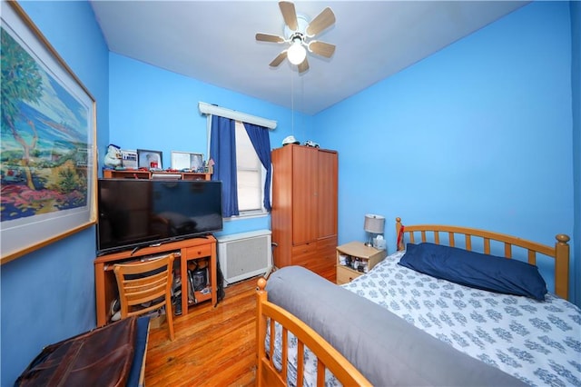 bedroom with ceiling fan, radiator heating unit, and wood finished floors