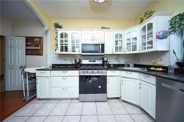 kitchen with decorative backsplash, dark countertops, glass insert cabinets, stainless steel appliances, and a sink