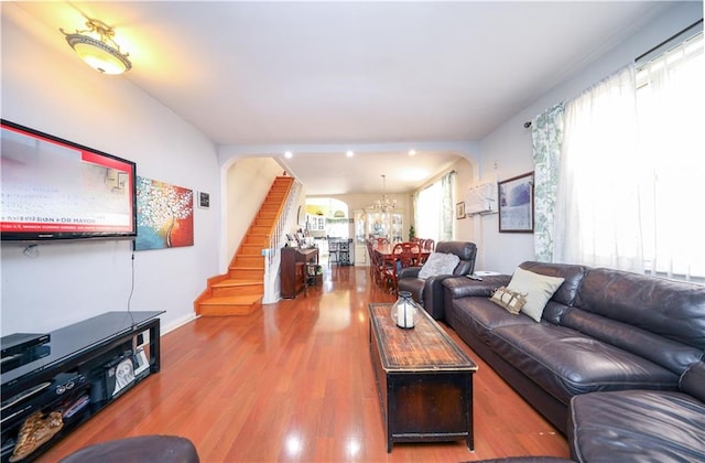 living area featuring stairs, arched walkways, wood finished floors, and a chandelier