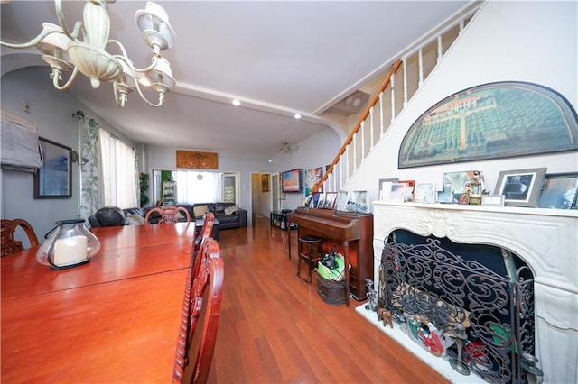 dining room featuring a fireplace, stairway, an inviting chandelier, and wood finished floors