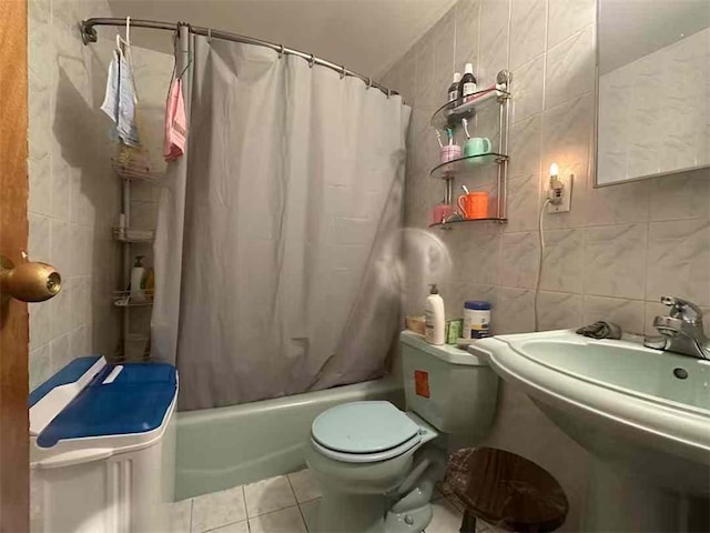 bathroom with tile walls, toilet, tile patterned floors, shower / bath combo with shower curtain, and a sink