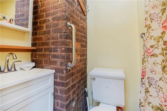 bathroom with brick wall, toilet, and vanity