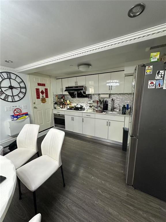 kitchen with ventilation hood, decorative backsplash, freestanding refrigerator, and white cabinetry