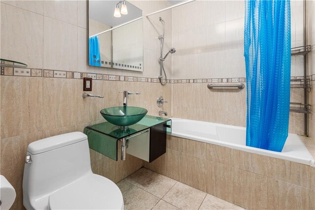 bathroom featuring tile patterned flooring, toilet, tiled shower / bath combo, tile walls, and a sink