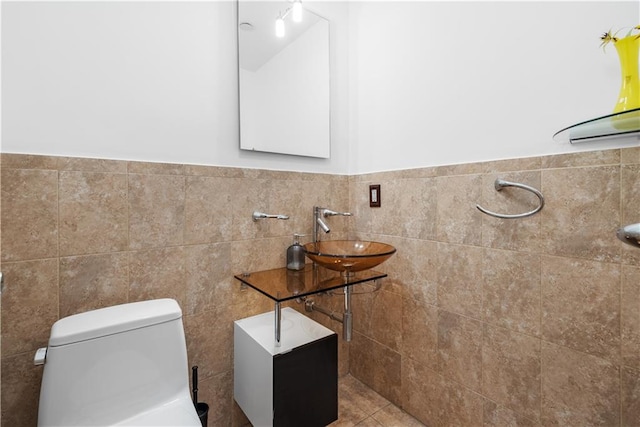 bathroom with tile walls, toilet, wainscoting, and a sink