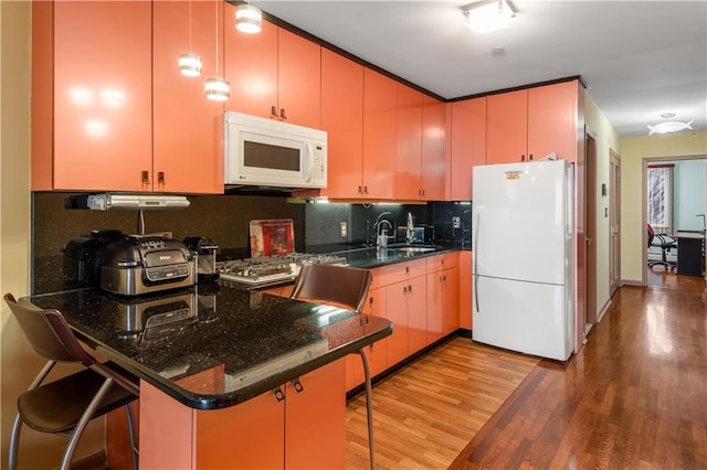 kitchen with white appliances, a peninsula, a sink, decorative backsplash, and light wood-type flooring