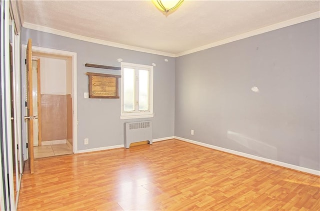 empty room with ornamental molding, light wood-type flooring, baseboards, and radiator heating unit