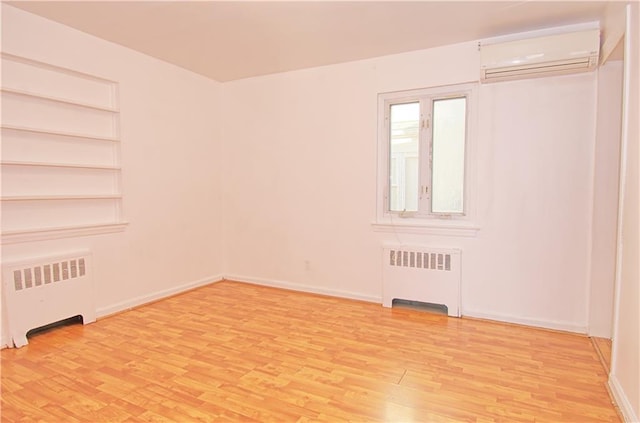 unfurnished room with an AC wall unit, radiator heating unit, built in shelves, and light wood-type flooring