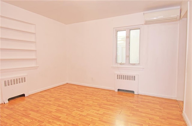 unfurnished room with radiator, light wood-style floors, baseboards, and a wall mounted air conditioner