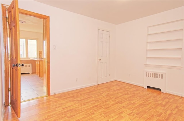 unfurnished room with baseboards, light wood finished floors, built in features, and radiator