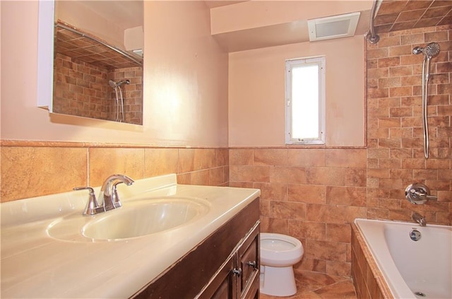 full bath with wainscoting, vanity, toilet, tiled shower / bath, and tile walls