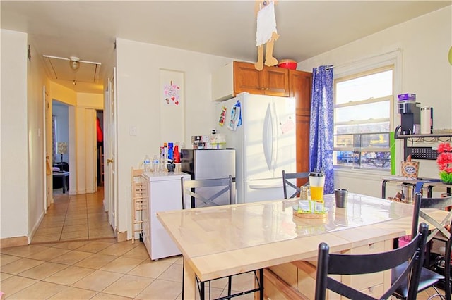 kitchen with light tile patterned floors, brown cabinets, and freestanding refrigerator