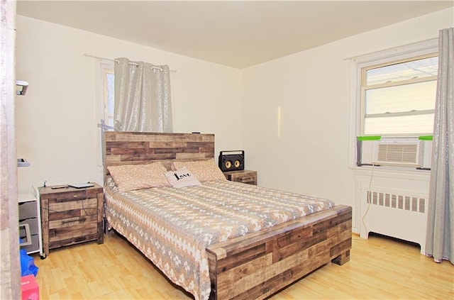 bedroom featuring cooling unit, radiator heating unit, and light wood-style floors