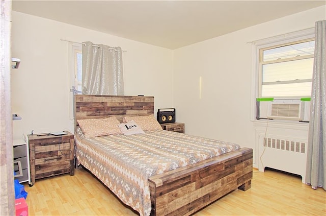 bedroom with radiator heating unit, light wood-style flooring, and cooling unit