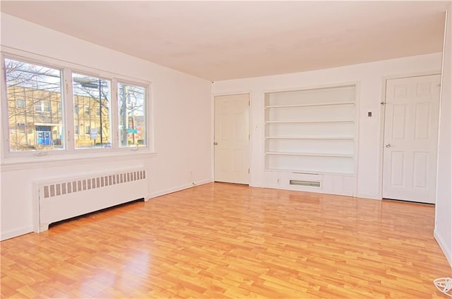 unfurnished room with baseboards, light wood-style floors, built in shelves, and radiator