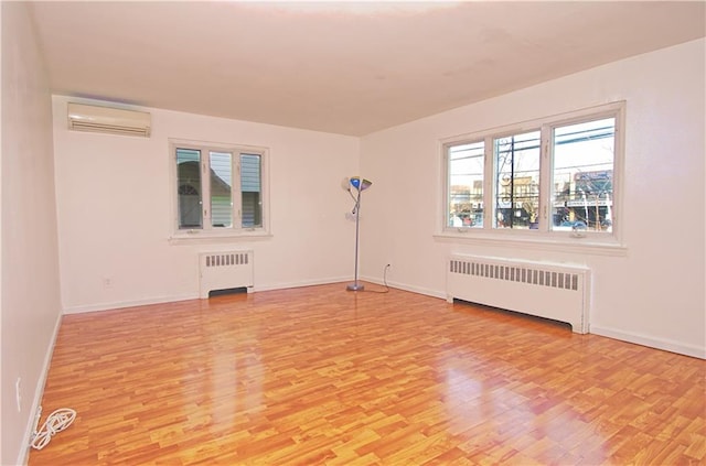 empty room featuring baseboards, radiator heating unit, a wall mounted air conditioner, and light wood-style floors