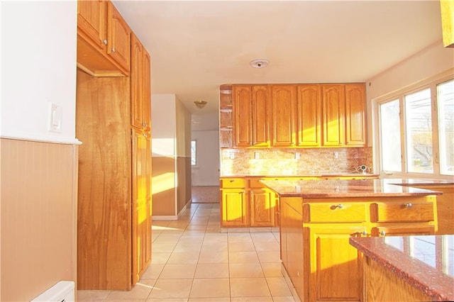 kitchen with light tile patterned floors, light stone counters, a baseboard heating unit, tasteful backsplash, and brown cabinetry