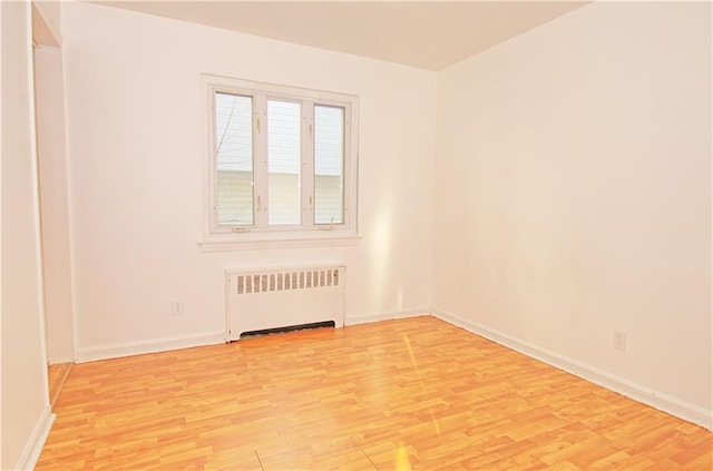 unfurnished room with baseboards, radiator, and light wood-type flooring