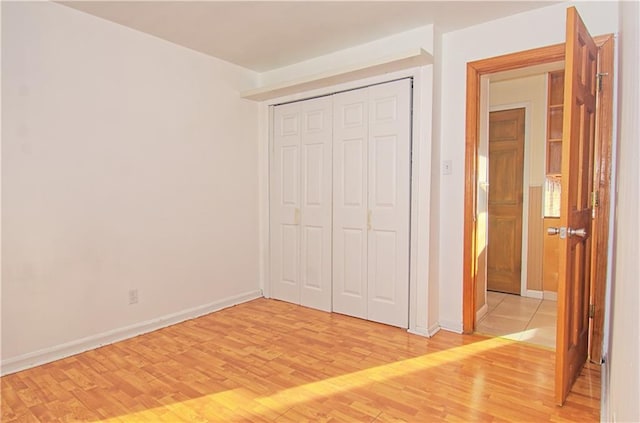 unfurnished bedroom with light wood-type flooring, baseboards, and a closet