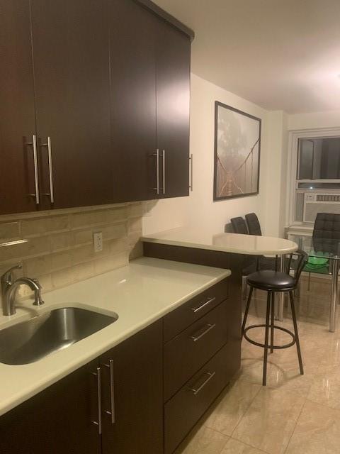 kitchen with decorative backsplash, a kitchen breakfast bar, a sink, and light countertops