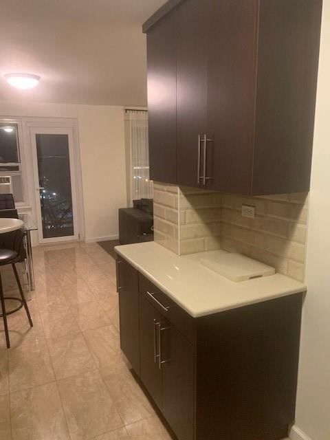 kitchen with decorative backsplash, baseboards, light countertops, and dark brown cabinets