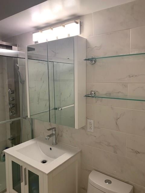 full bath featuring toilet, a shower stall, tile walls, and vanity