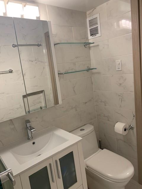 bathroom with tile walls, visible vents, vanity, and toilet