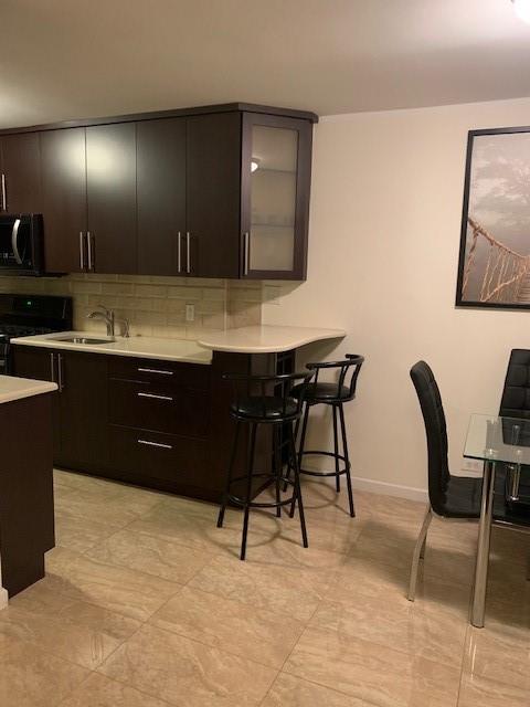 kitchen featuring light countertops, backsplash, black range with gas stovetop, a sink, and a kitchen breakfast bar