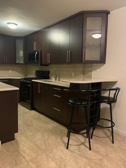 kitchen featuring light countertops, backsplash, stainless steel microwave, gas stove, and glass insert cabinets