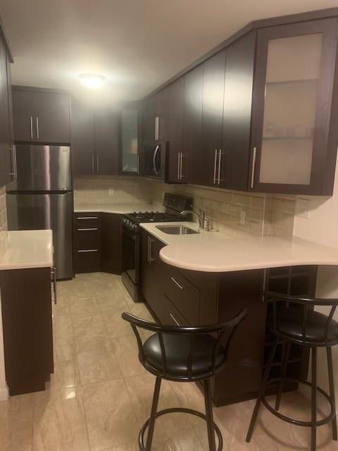 kitchen featuring a sink, appliances with stainless steel finishes, backsplash, a kitchen bar, and glass insert cabinets