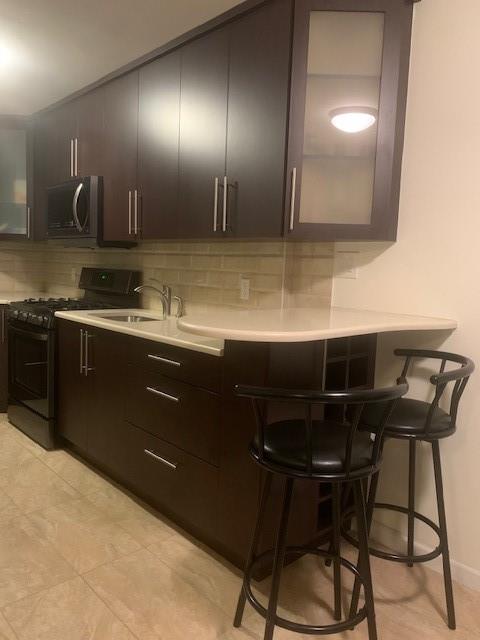 kitchen with tasteful backsplash, light countertops, appliances with stainless steel finishes, glass insert cabinets, and a kitchen bar