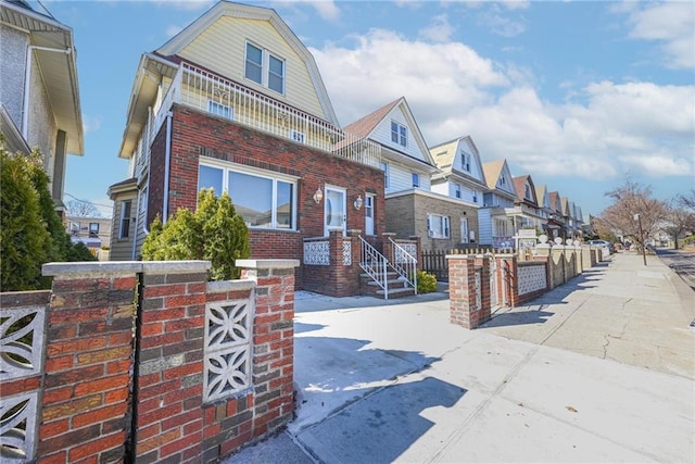 view of front of house featuring a gambrel roof, a residential view, brick siding, and fence