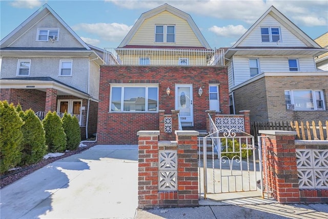 view of front facade featuring a fenced front yard, a gate, a gambrel roof, and brick siding