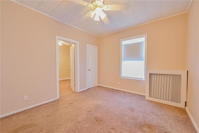 carpeted spare room featuring ornamental molding, a ceiling fan, and baseboards