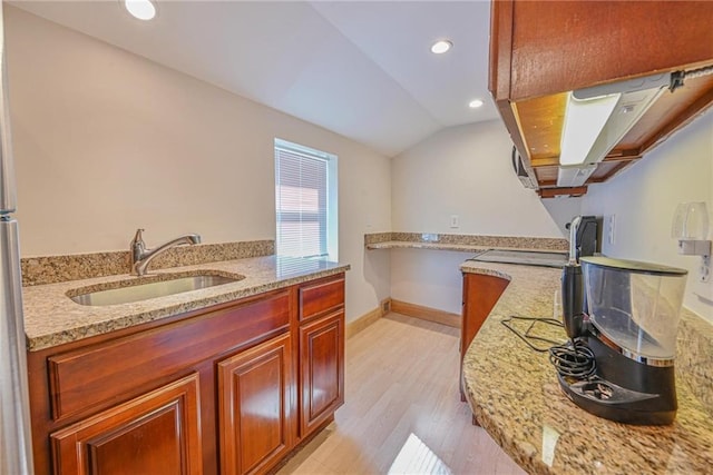 kitchen with a sink, light wood-style flooring, light stone counters, lofted ceiling, and baseboards