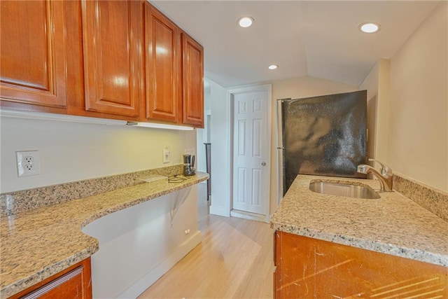 kitchen with a sink, light wood-style flooring, light stone counters, recessed lighting, and brown cabinetry