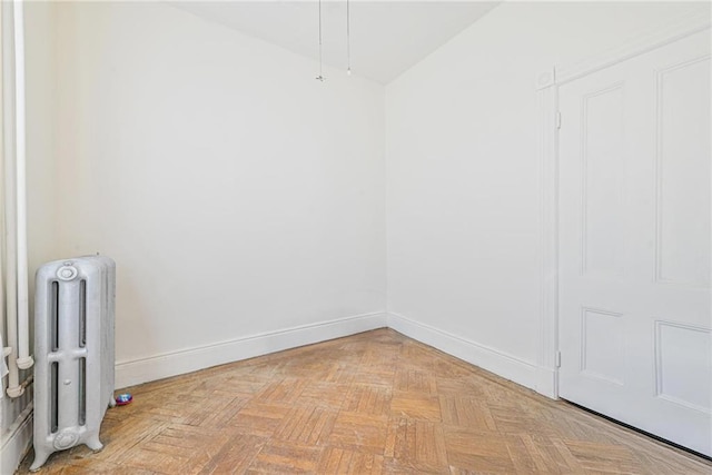 empty room with baseboards, radiator heating unit, and vaulted ceiling