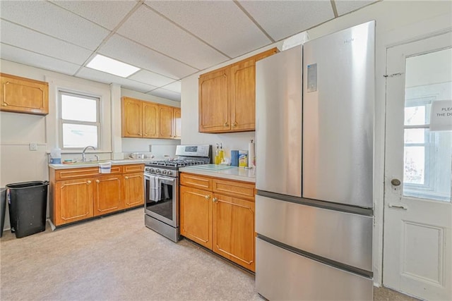kitchen with a sink, stainless steel appliances, light countertops, a drop ceiling, and light carpet