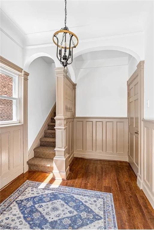 interior space featuring arched walkways, a chandelier, a wainscoted wall, stairway, and dark wood finished floors