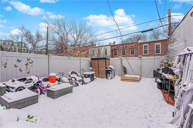 yard covered in snow featuring an outbuilding, a fenced backyard, and a shed