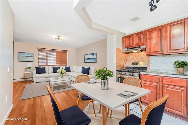 kitchen featuring stainless steel gas range oven, under cabinet range hood, open floor plan, light countertops, and decorative backsplash