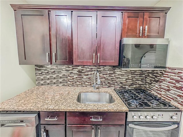 kitchen with backsplash, appliances with stainless steel finishes, light stone countertops, and a sink