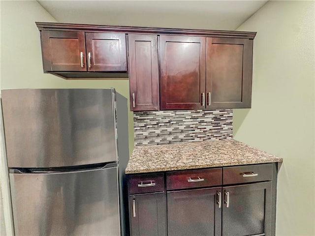 kitchen with dark brown cabinetry, backsplash, freestanding refrigerator, and light stone countertops